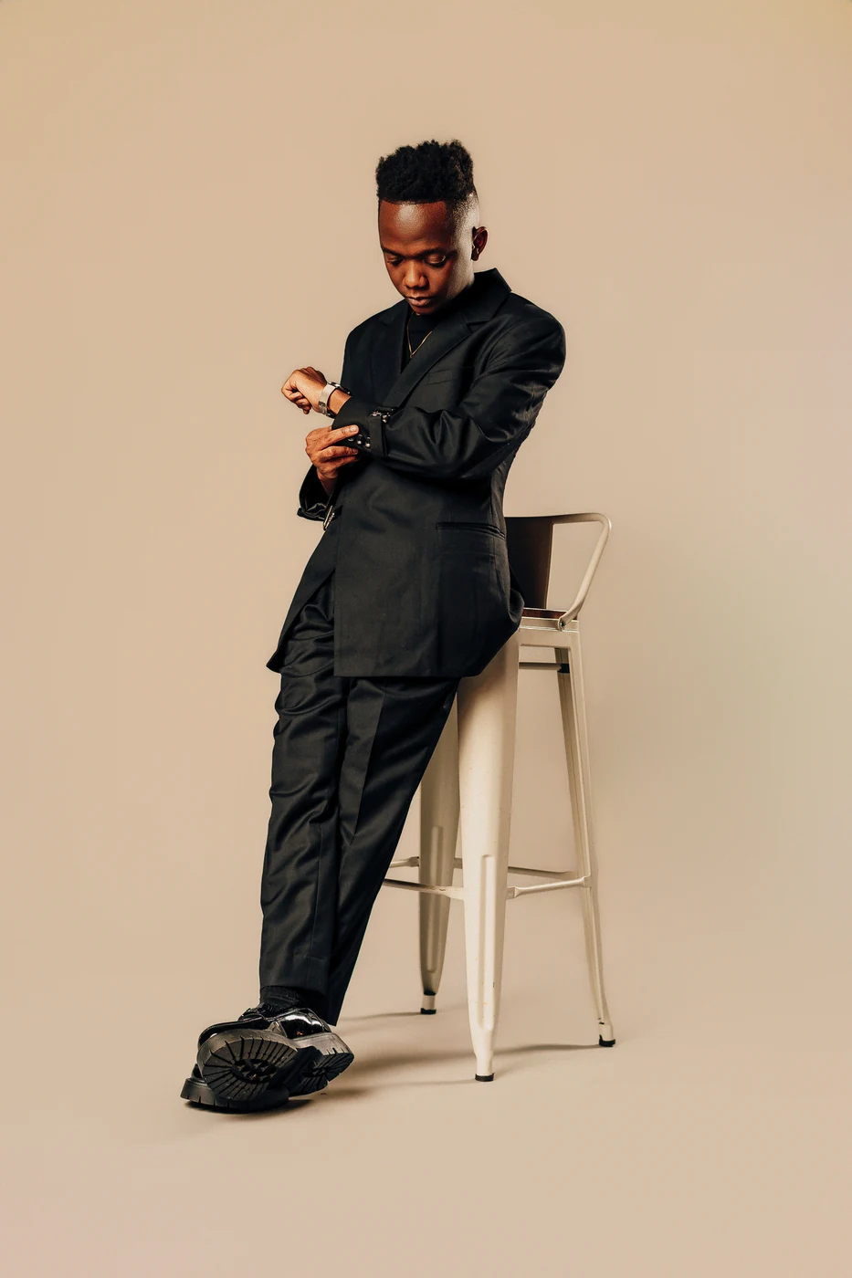 Viny standing beside a stool in a black suit